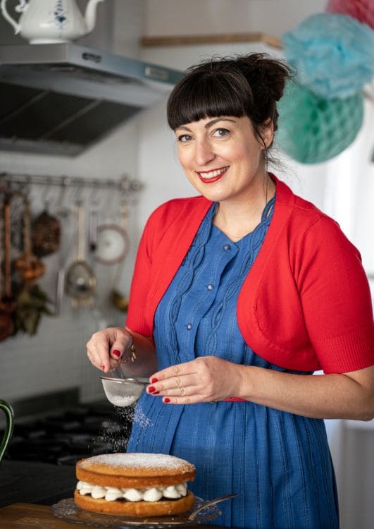 Chef Anne Faber sprinkling powdered sugar over a cake in ChefPassport Anne's Kitchen